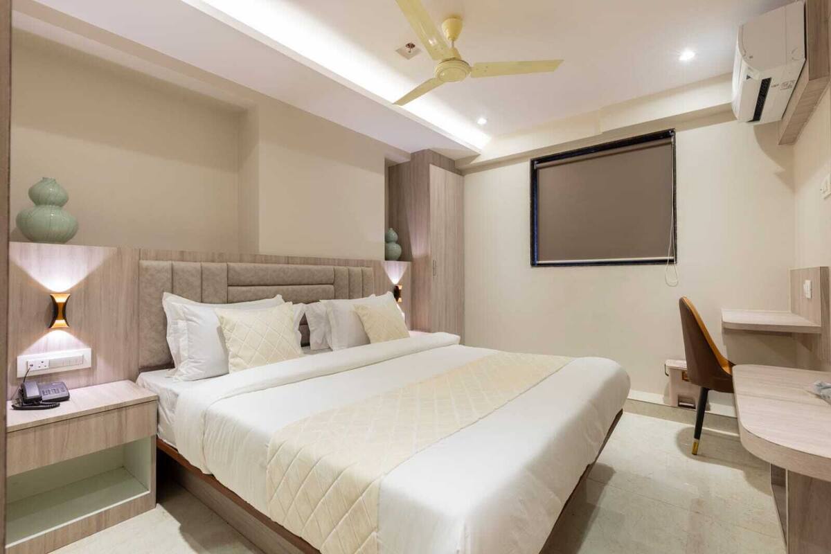 Quarto de hotel moderno com uma cama grande, abajures, ventoinha no teto, escrivaninha com cadeira e ar condicionado.