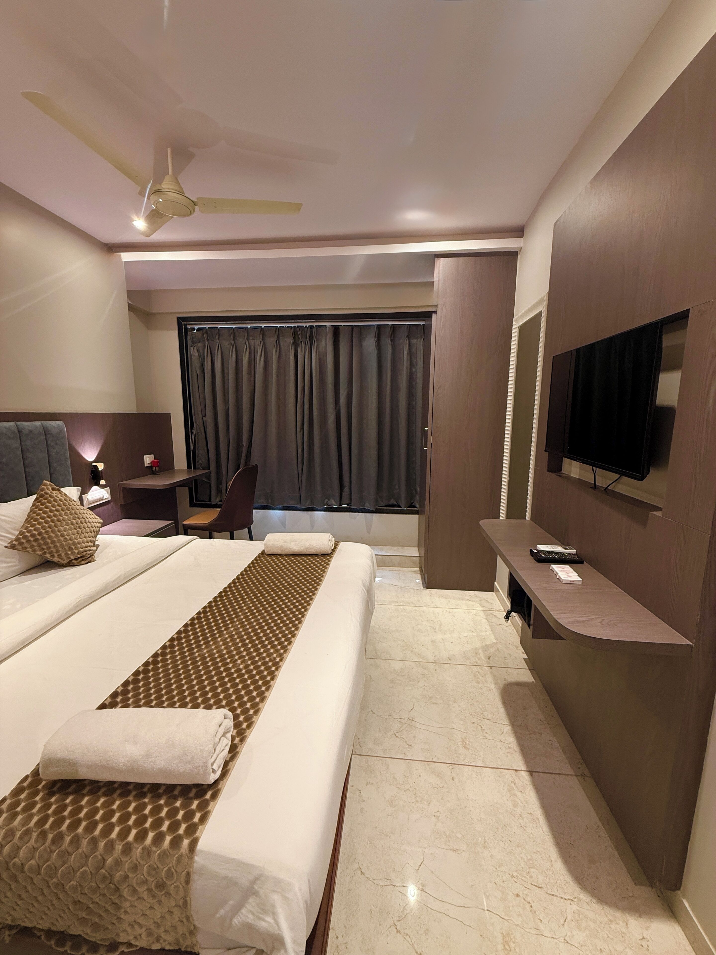 Ein modernes Hotelzimmer mit einem großen Bett, einem Schreibtisch, einem Fernseher und einem Deckenventilator.