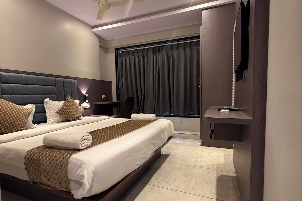 Quarto de hotel moderno com uma cama grande, um ventilador de teto, uma TV fixada na parede e uma mesinha de cabeceira.