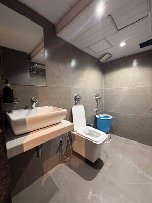 A modern bathroom with a large sink, toilet, and blue trash bin. - kurla suites (Mumbai)