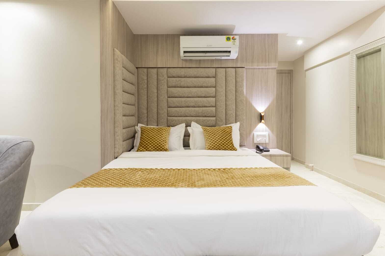 A modern hotel room with a large bed, a bedside table with a lamp, and an air conditioning unit above the bed.