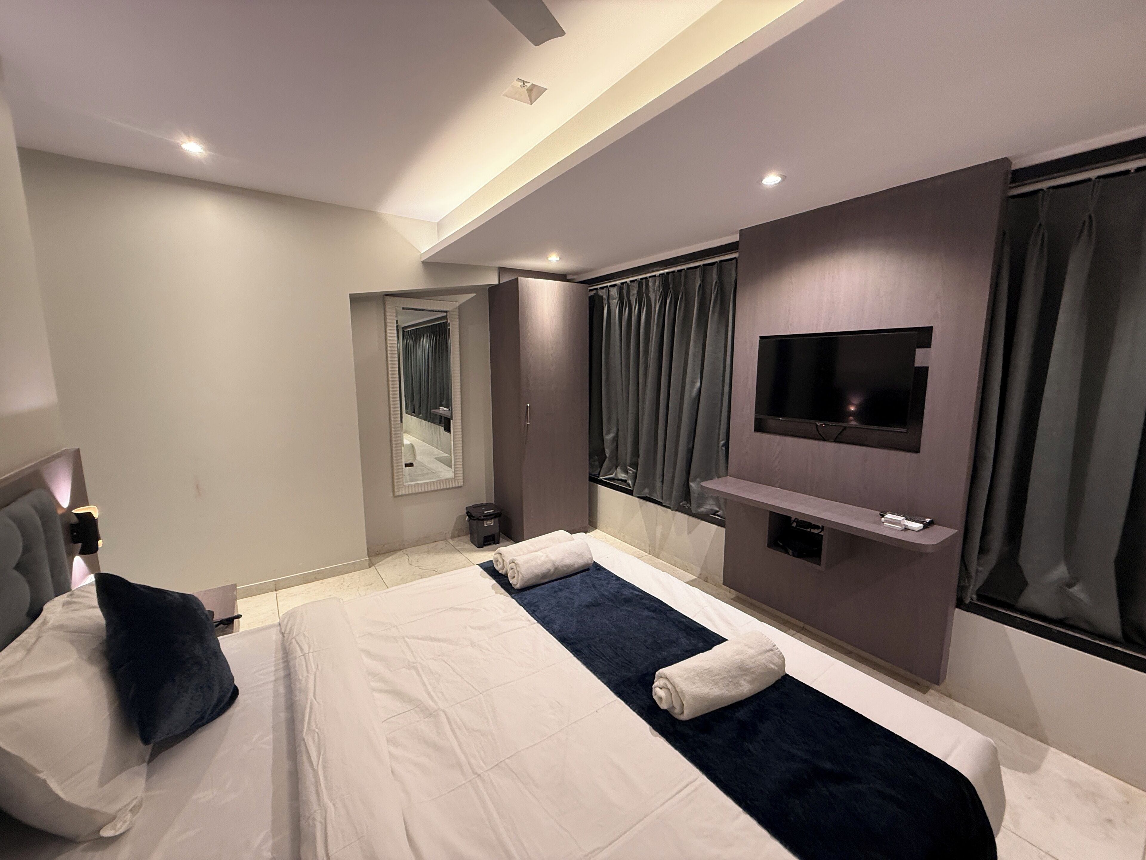 A modern hotel room with two beds, a TV, a mirror, and a window with curtains.