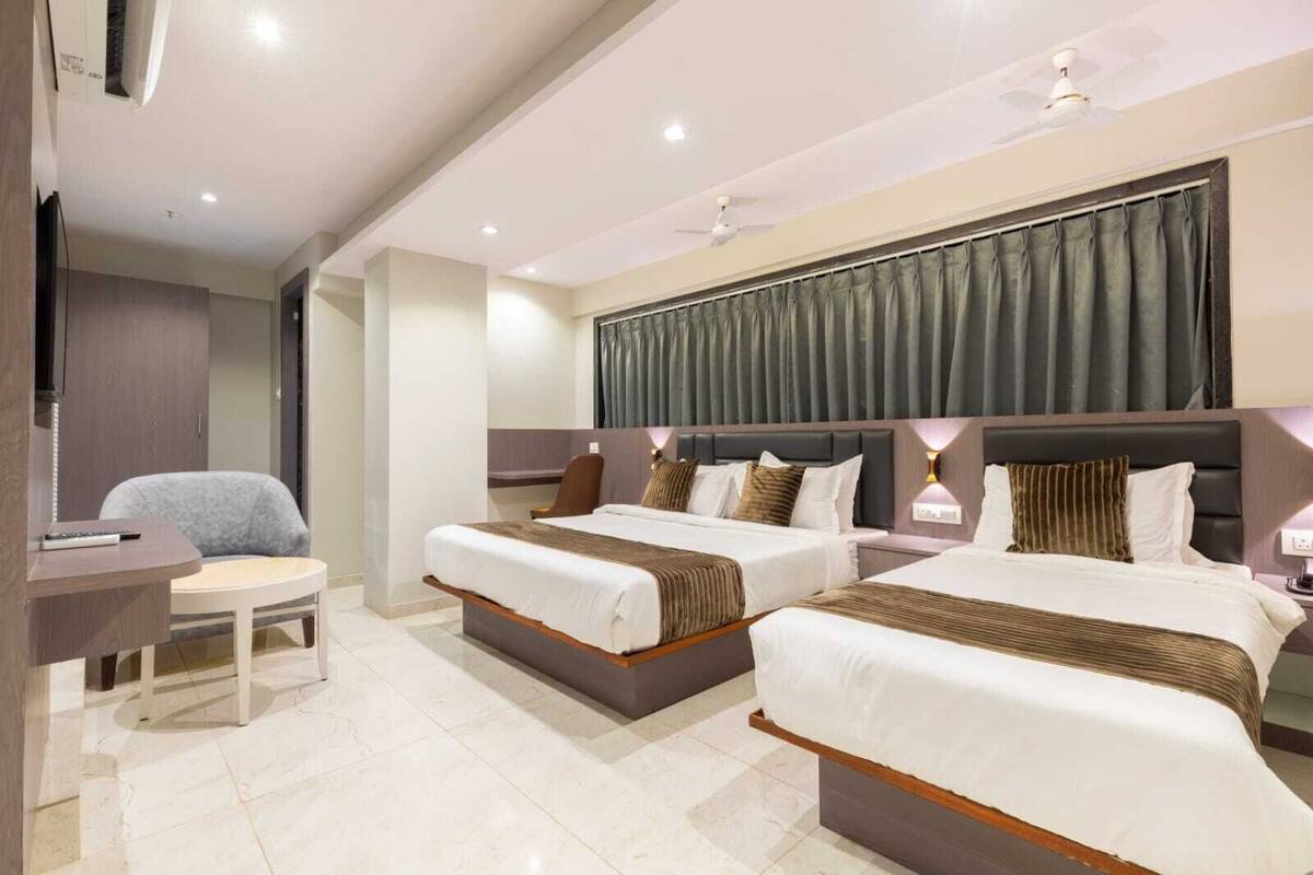 Quarto de hotel com duas camas, uma escrivaninha, uma cadeira e um ventilador de teto.