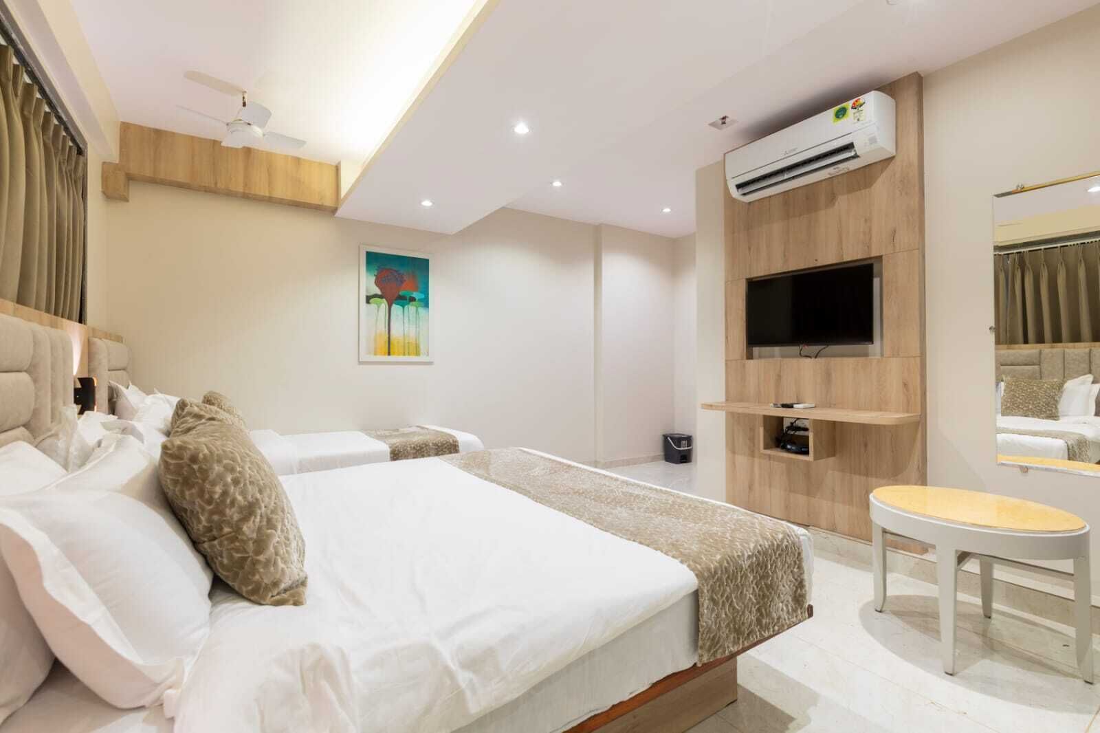 A hotel room with a bed, a TV, an air conditioning unit, and a small table.