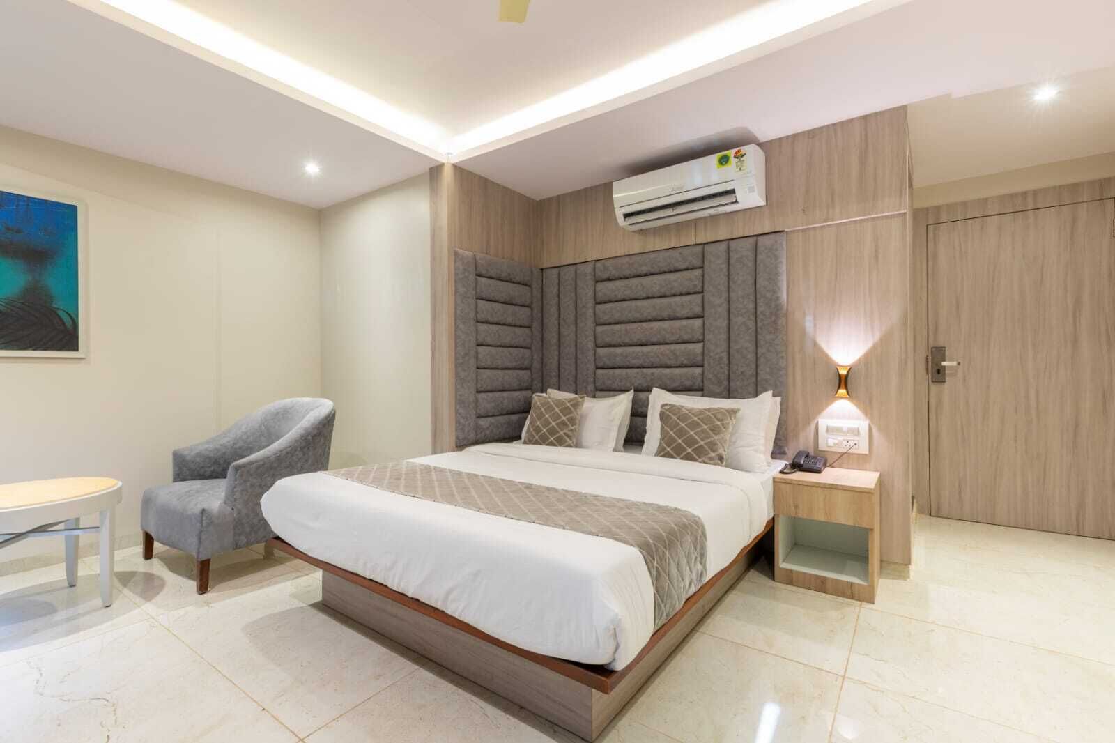 Une chambre d’hôtel moderne équipée d’un grand lit, d’une chaise, d’un climatiseur, d’une lampe de chevet et d’une armoire.