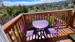 A wooden deck with a table and two chairs, overlooking a scenic landscape with hills and vegetation.