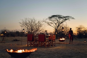 An outdoor dining setup with chairs and tables, a fire pit, and lanterns.