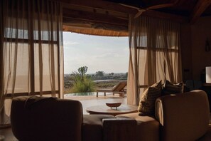 A room with a sofa and a table, a window with curtains, and a view of the outdoors.