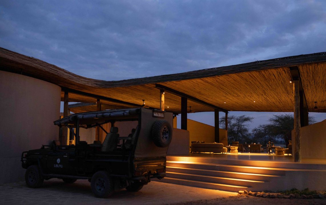 A safari vehicle parked under a covered area with steps leading to an outdoor seating area.