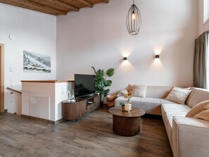 Ein modernes Wohnzimmer mit Holzboden, einer Couch, einem Couchtisch, einem Fernseher und einer Pflanze.