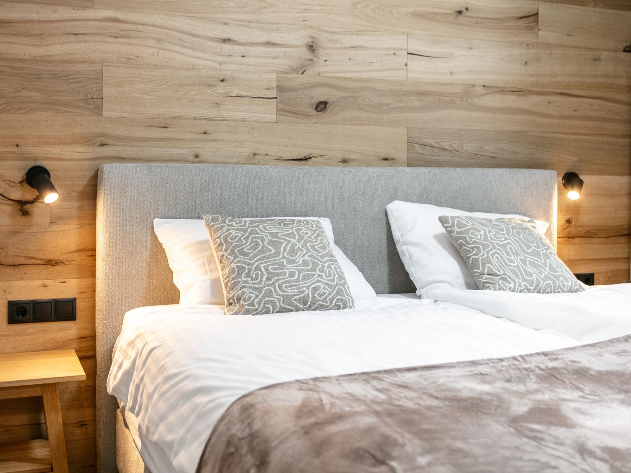 Een net opgemaakt bed met gestreepte kussens, een houten hoofdbord en wandlampen.