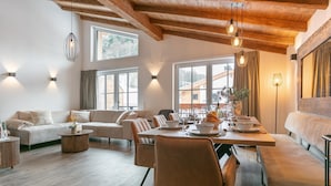 Uma sala de estar ampla com teto de madeira, uma mesa de jantar posta para quatro pessoas e um sofá.