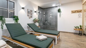 Uma sala de spa moderna com duas macas de massagem verdes, um box de chuveiro em vidro e piso de madeira.