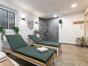 A modern spa room with two green massage beds, a glass shower enclosure, and wooden flooring.
