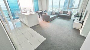 A modern living room with a grey sofa, a small dining table, and a kitchen area with a white countertop and a glass bowl. - Hilton Surfers Paradise 3 bedroom 2 bathroom ocean and river views (Surfers Paradise)