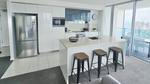A modern kitchen with a stainless steel refrigerator, white cabinetry, and a large island with stools. - Hilton Surfers Paradise 3 bedroom 2 bathroom ocean and river views (Surfers Paradise)