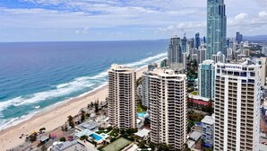 A coastal cityscape with high-rise buildings, including a Novotel hotel, overlooking a beach and the ocean. - Hilton Surfers Paradise 3 bedroom 2 bathroom ocean and river views (Surfers Paradise)