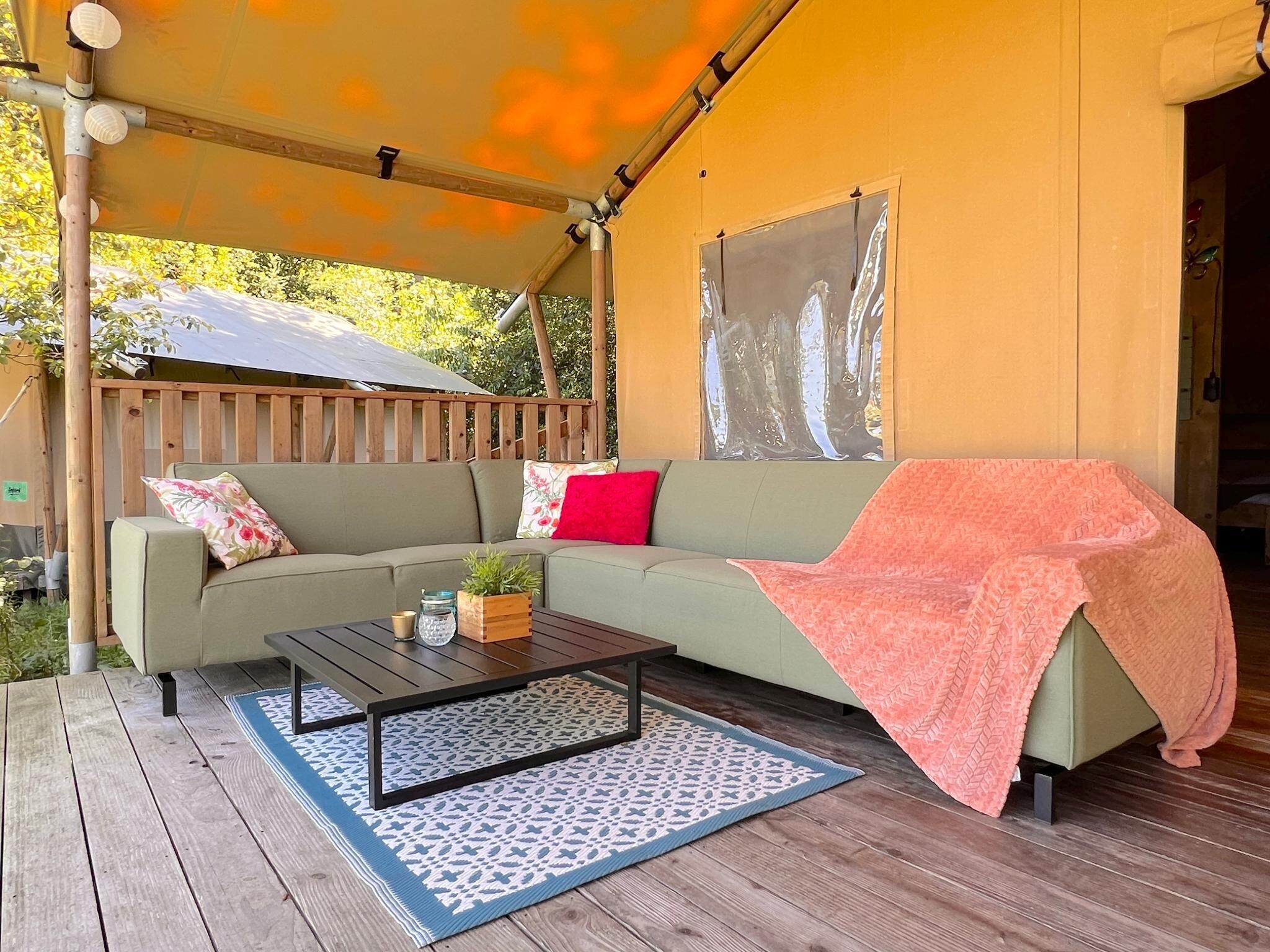 A covered outdoor seating area with a sofa, a coffee table, and a blanket.