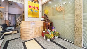 Zona de recepción de un hotel con un mostrador de madera, un sofá y varias plantas.