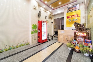 A hotel lobby with a Coca-Cola refrigerator, a reception desk with a statue, and a sign that reads "HOTEL Yg Anis." - Collection O Vy Anh - Binh Tan District (Ho-Chi-Minh)