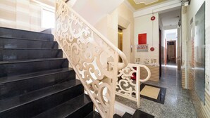 Una escalera con peldaños negros y barandillas blancas ornamentales, que conduce a una habitación con piso de baldosas y un cartel rojo en la pared.