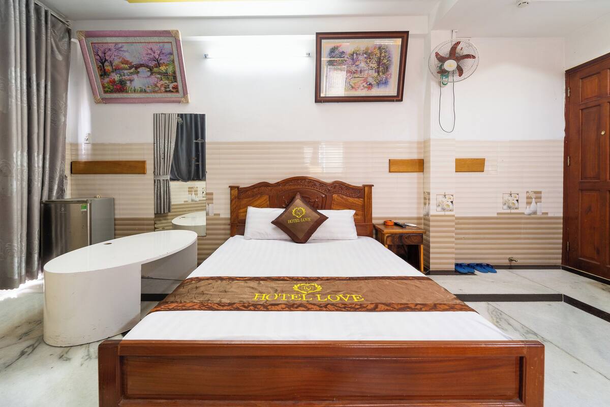 A hotel room with a bed, a vanity, a sink, and a fan.