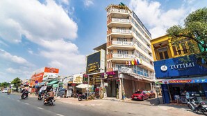 Un hotel de varios pisos con balcones, una cafetería y varias tiendas a lo largo de una calle concurrida.