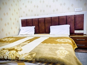 A hotel room with a large bed, two pillows, a wooden nightstand, and a wall with patterned wallpaper. - radhika comfort stay (Vrindavan)
