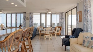 Un'ampia zona giorno con tavolo da pranzo, sedie in vimini, divano e grandi finestre con vista.