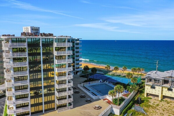 A high-rise hotel with multiple balconies, a pool, and a beach view.