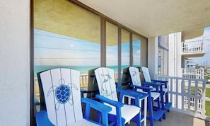 A balcony with blue chairs and a large window overlooking the ocean.