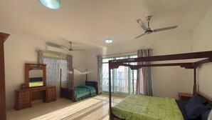 A bedroom with a four-poster bed, a wooden dresser, a vanity with a mirror, and a ceiling fan. - Mango Beach Hotel (Chukwani)