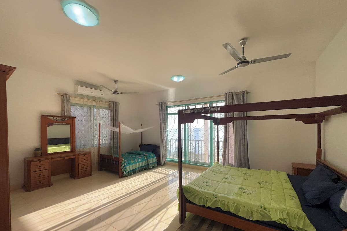 A bedroom with a four-poster bed, a wooden dresser, a vanity with a mirror, and a ceiling fan.