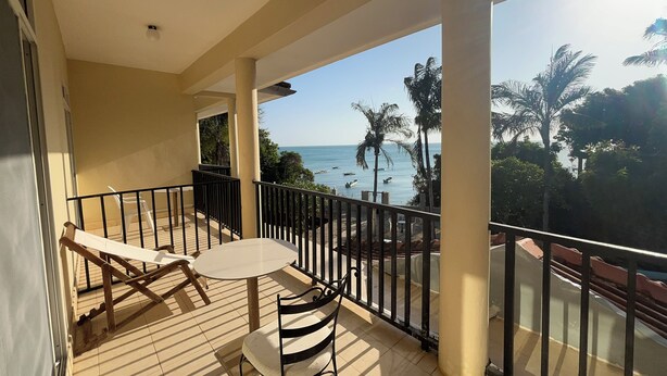 A balcony with a table and chairs, overlooking a beach with palm trees and boats. - Mango Beach Hotel (Chukwani)
