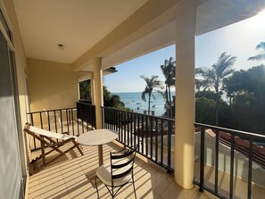 A balcony with a table and chairs, overlooking a beach with palm trees and boats. - Mango Beach Hotel (Chukwani)