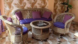 A wicker sofa set with patterned cushions, a round coffee table, and a potted plant in a room with patterned wallpaper and checkered flooring. - K2view Retreat (Darjeeling)