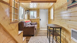 A wooden cabin interior with a brown leather sofa, a small table, and a door. - Cute Couple's Tiny Home, 8 Mi to Downtown Helena! (East Helena)