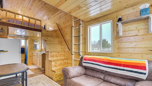 A cozy cabin interior with a wooden interior, a sofa, a dining table, and a kitchen area. - Cute Couple's Tiny Home, 8 Mi to Downtown Helena! (East Helena)