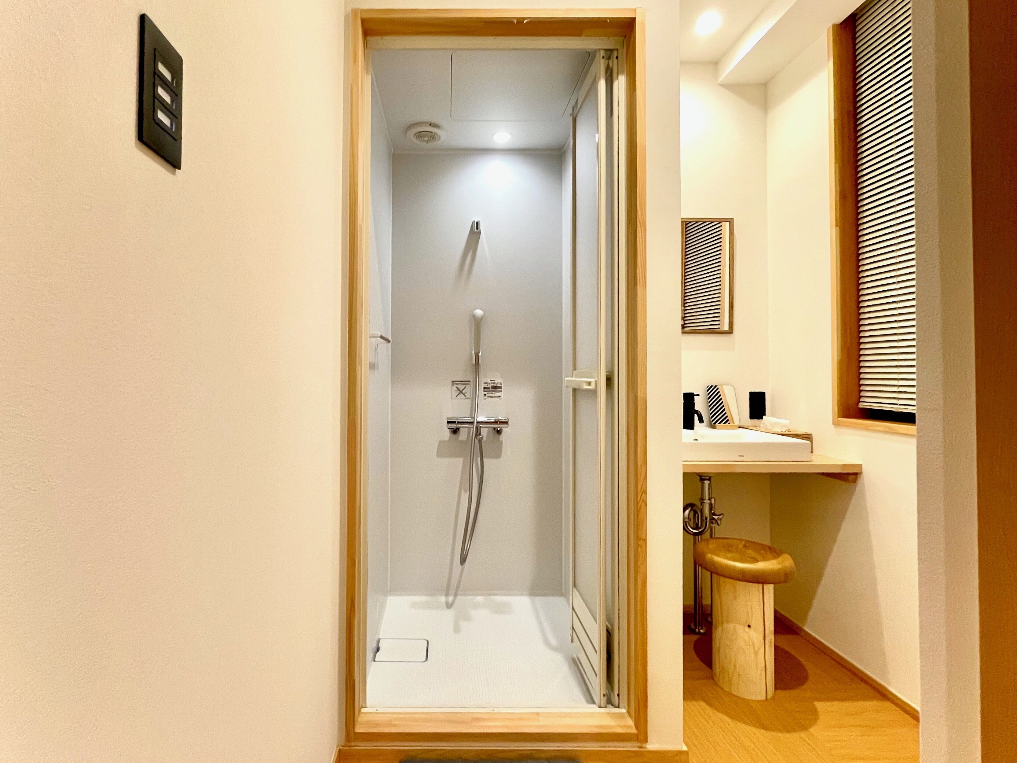 Eine Dusche mit Glastür, ein Holzschemel und ein kleines Waschbecken mit Spiegel darüber.