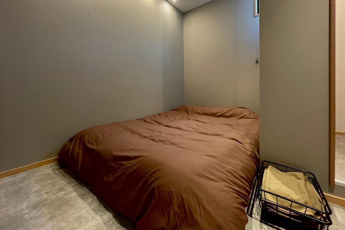 A room with a single bed, a small window, and a wall-mounted light fixture.
