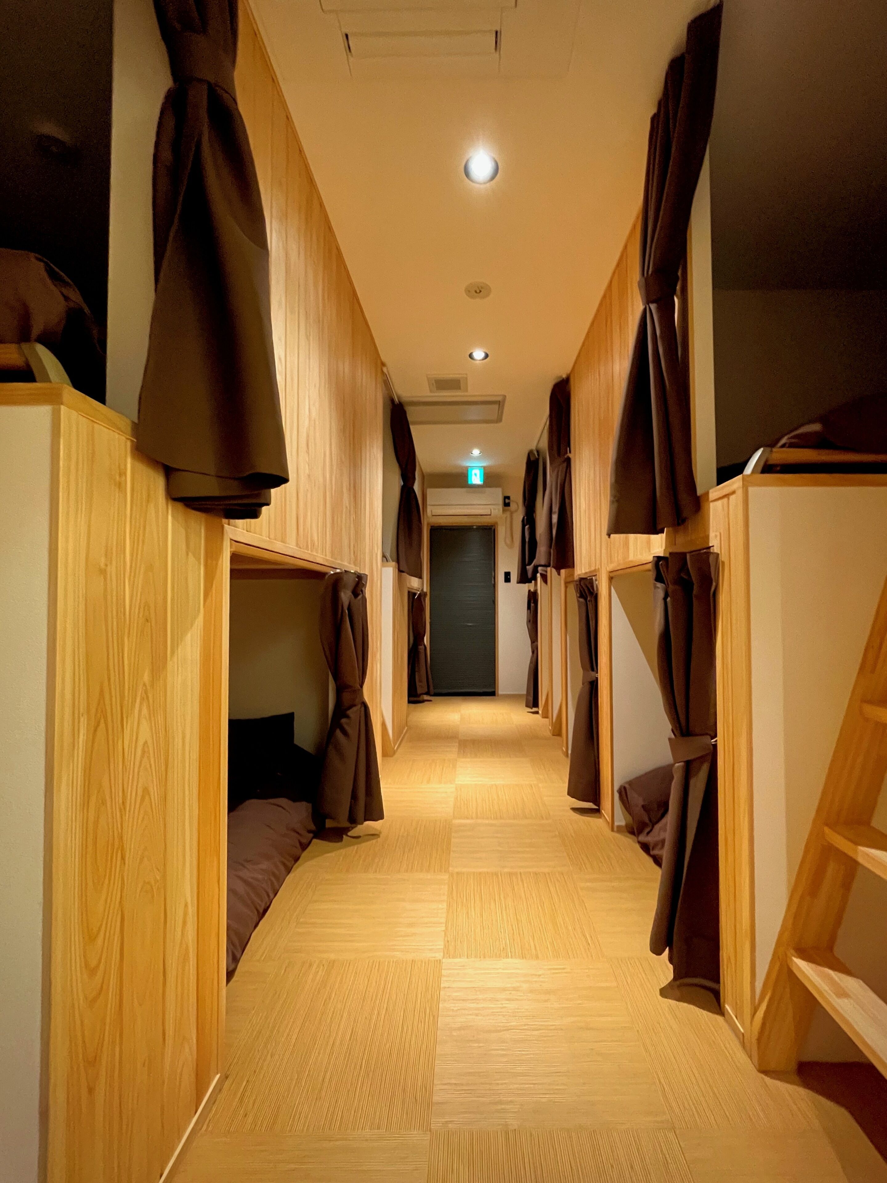 A corridor with bunk beds, wooden flooring, and a ceiling light.