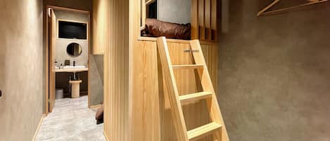 Una habitación con literas, una escalera de madera, un baño pequeño y un armario de madera.