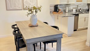 Moderni keittiö, jossa on valkoiset kaapit, graniittitaso sekä ruokailutila, jossa on puinen pöytä ja tuolit.