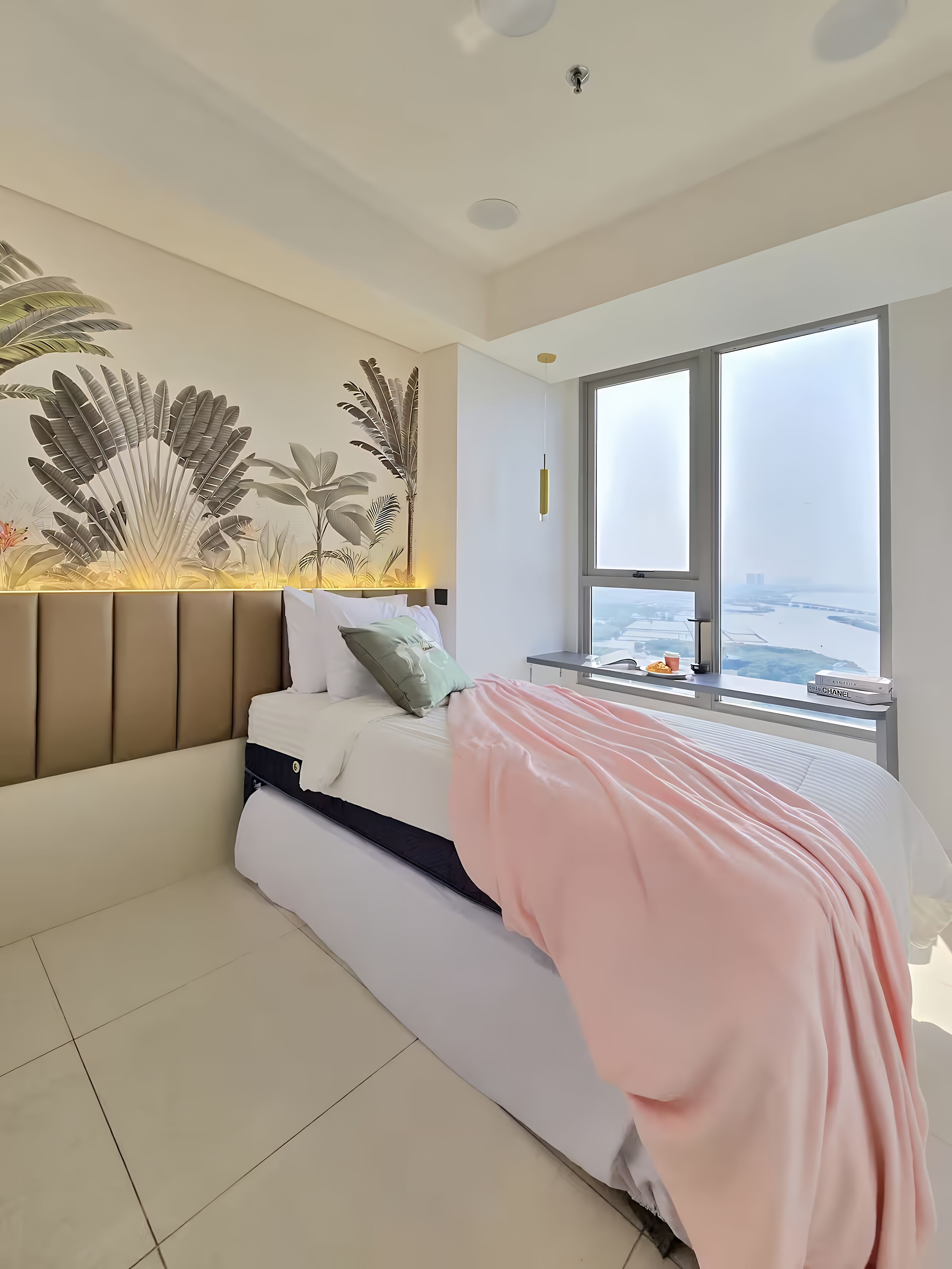 Un dormitorio moderno con una cama, un ventanal grande y una decoración vegetal en la pared.