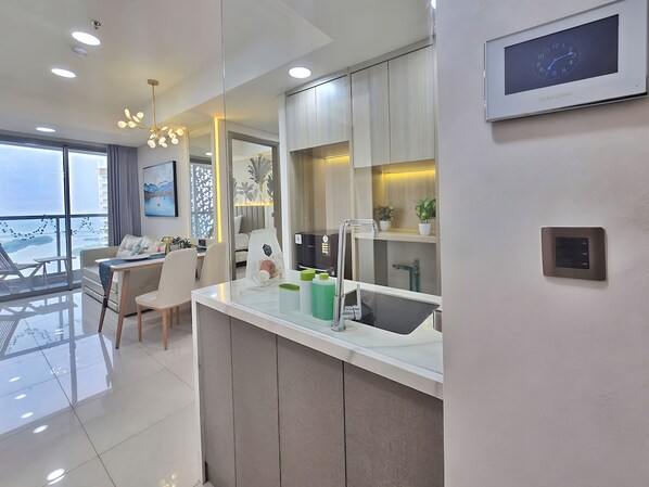 A modern kitchen with a built-in sink, a dining area with a table and chairs, and a large window offering a view. - By The Bay By SanLiving - 3BR - PIK (Jakarta)