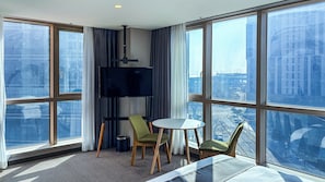 A high-rise hotel room with a large window, a flat-screen TV, a small round table, two chairs, and a bed. - Centum Suite Hotel (Busan)