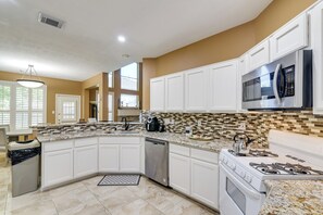 A kitchen with white cabinets, a stainless steel dishwasher, a gas stove, and a microwave. - 3,500-Sq-Ft Retreat w/ Private Yard in Sugar Land! (Sugar Land)