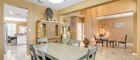 A spacious dining area with a large table and chairs, a decorative cabinet, and a chandelier.