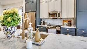 A modern kitchen with dark grey cabinets, stainless steel appliances, and a marble countertop. - Designer Wheeler Retreat: Walk to Dining! (Oklahoma City)