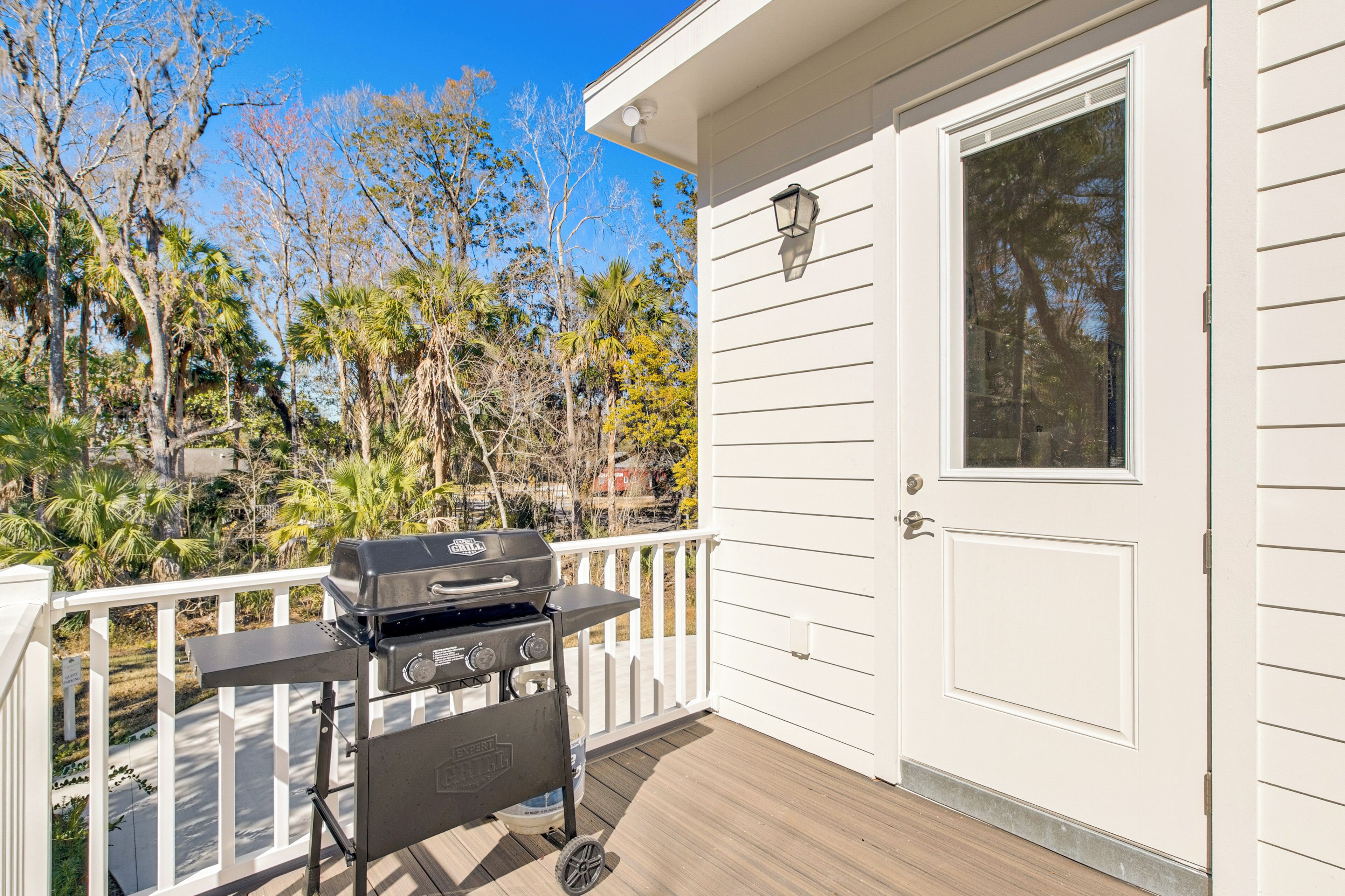 A deck with a grill, a white door, and a view of trees and a clear sky.